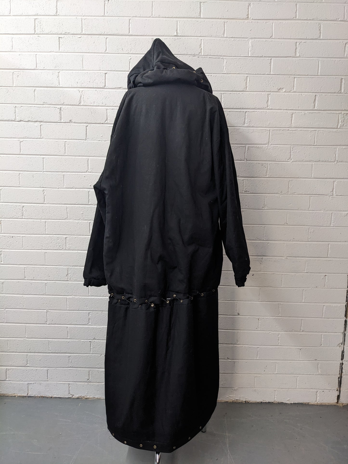 Black modular coat with hood on dress form in front of brick wall
