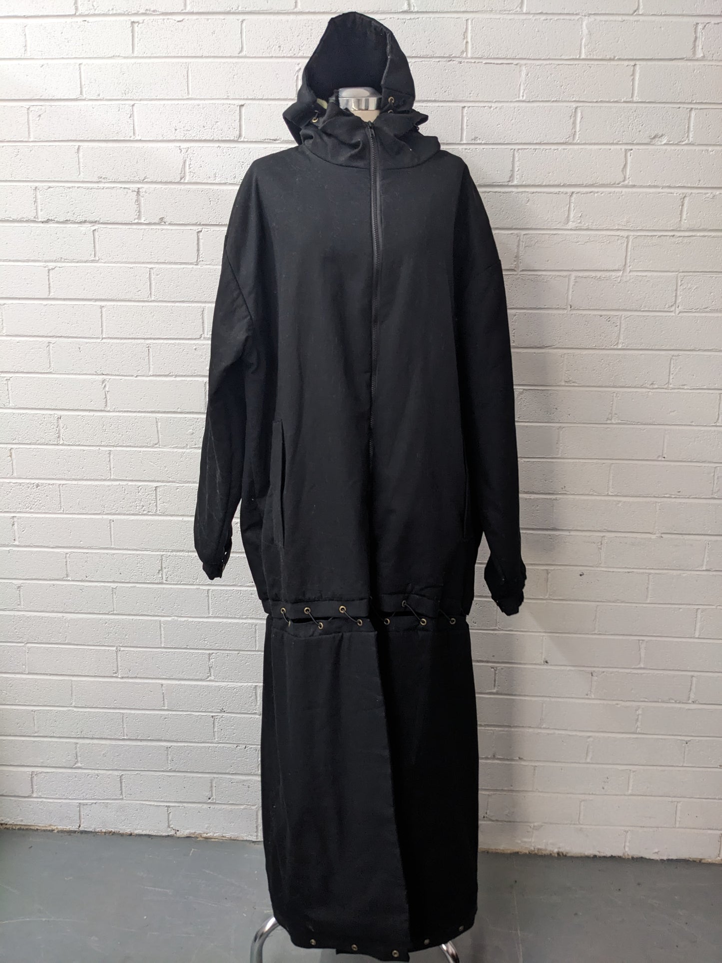 Black modular coat with hood on dress form in front of brick wall