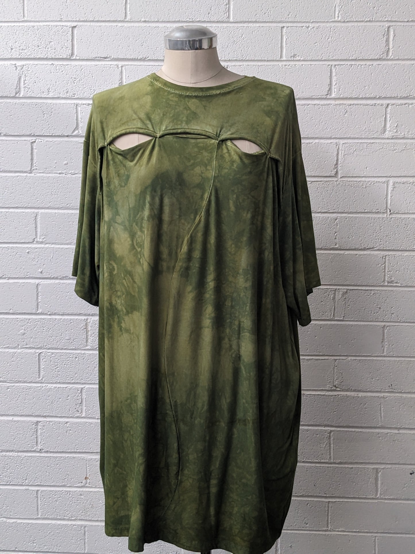 Green shirt with cutouts on mannequin against brick wall