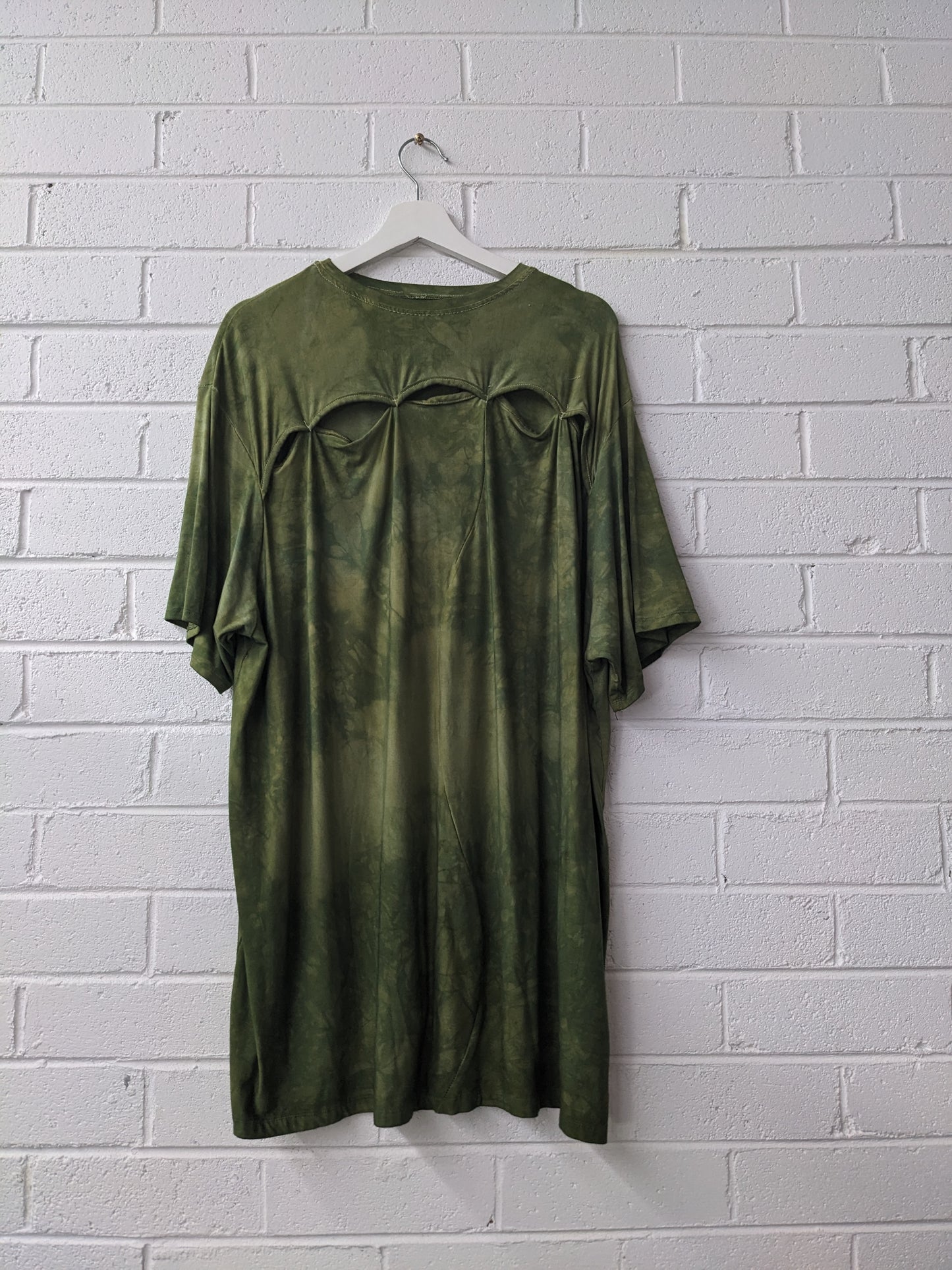 Green dress on a hanger against a white brick wall