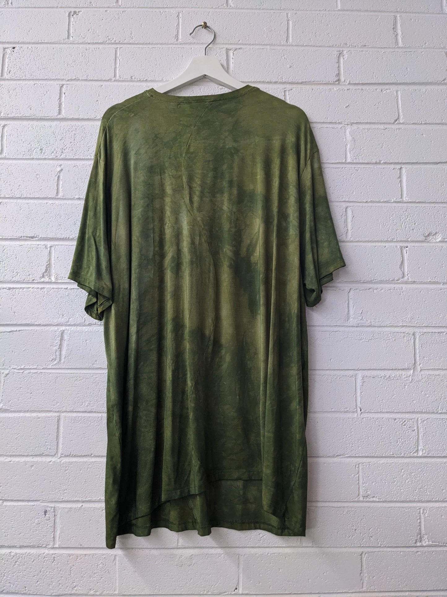 Green t-shirt on a hanger against a white brick wall