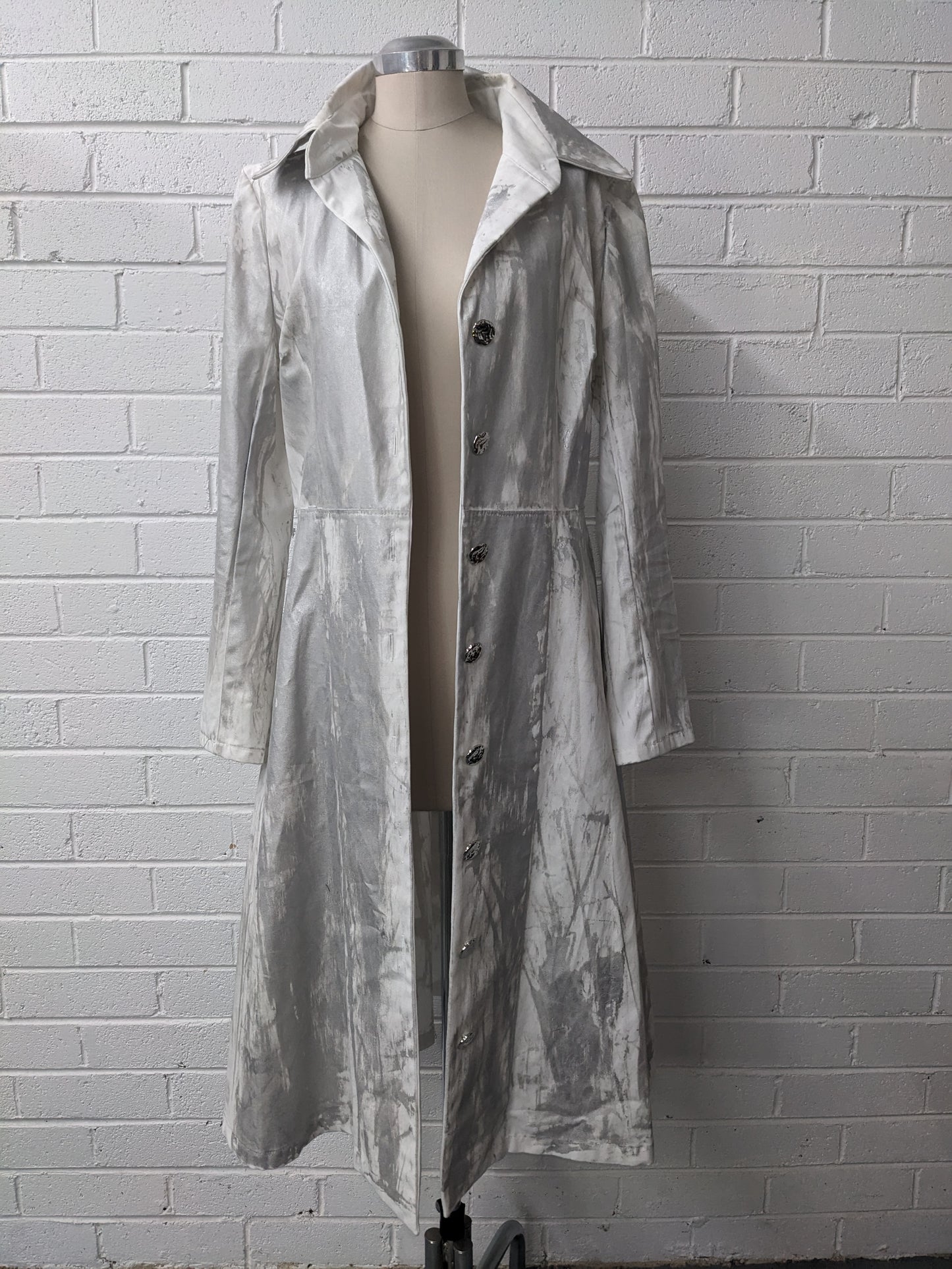 Long silver coat on mannequin against brick wall