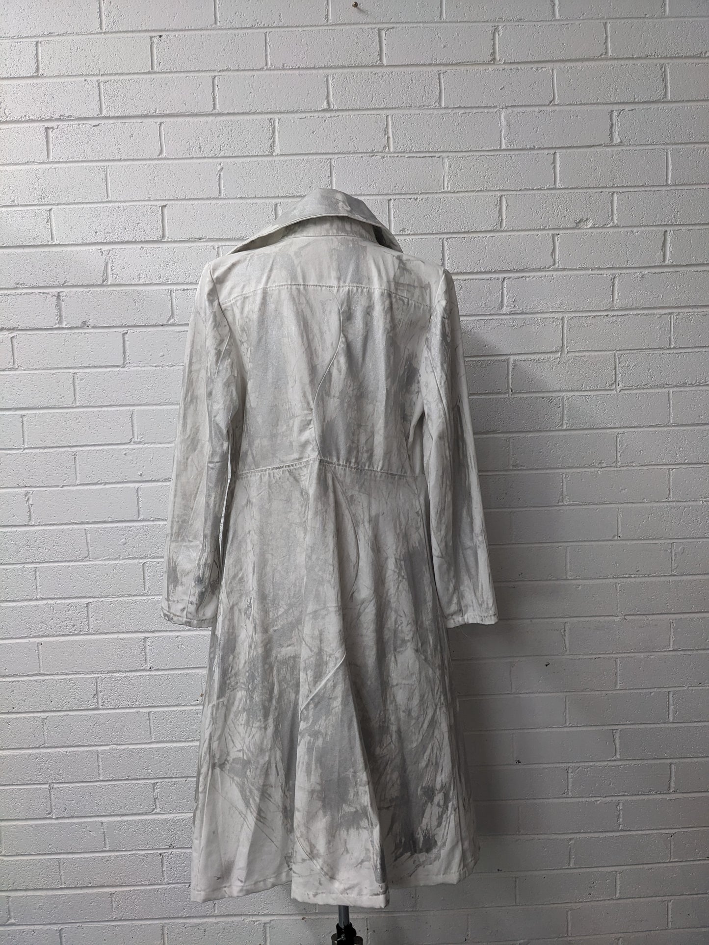 Long silver coat on mannequin against brick wall