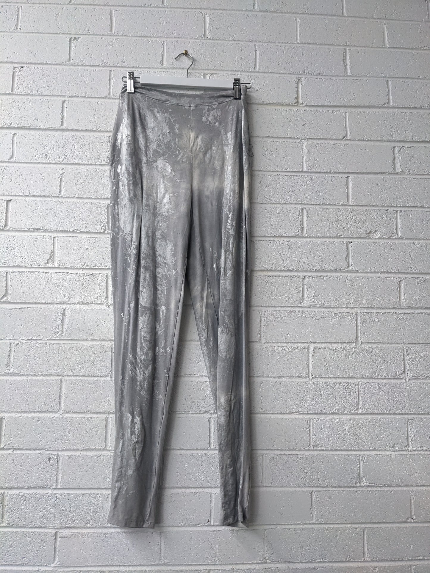 Silver metallic pants hanging against a white brick wall