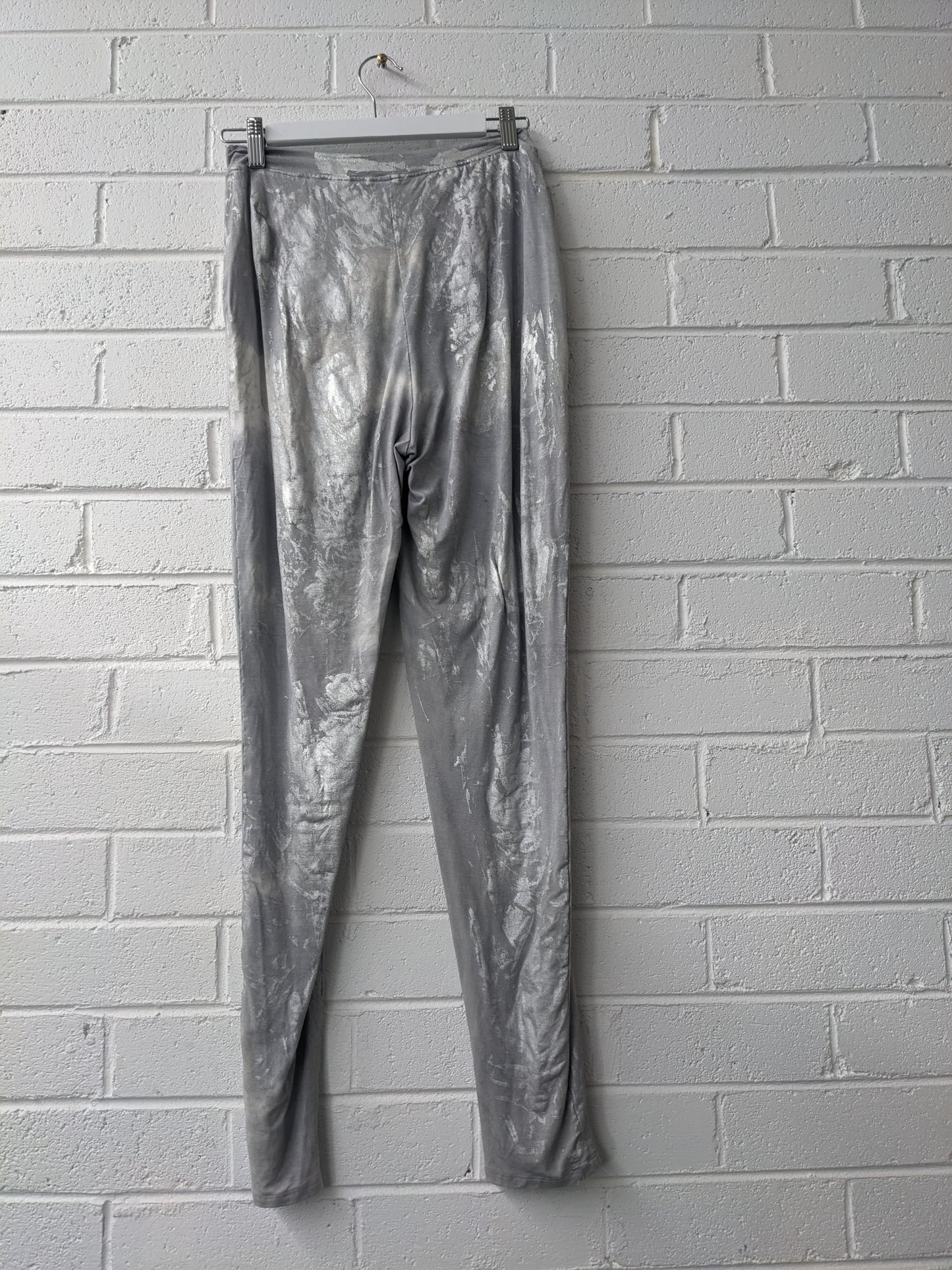 Silver metallic pants hanging against a white brick wall