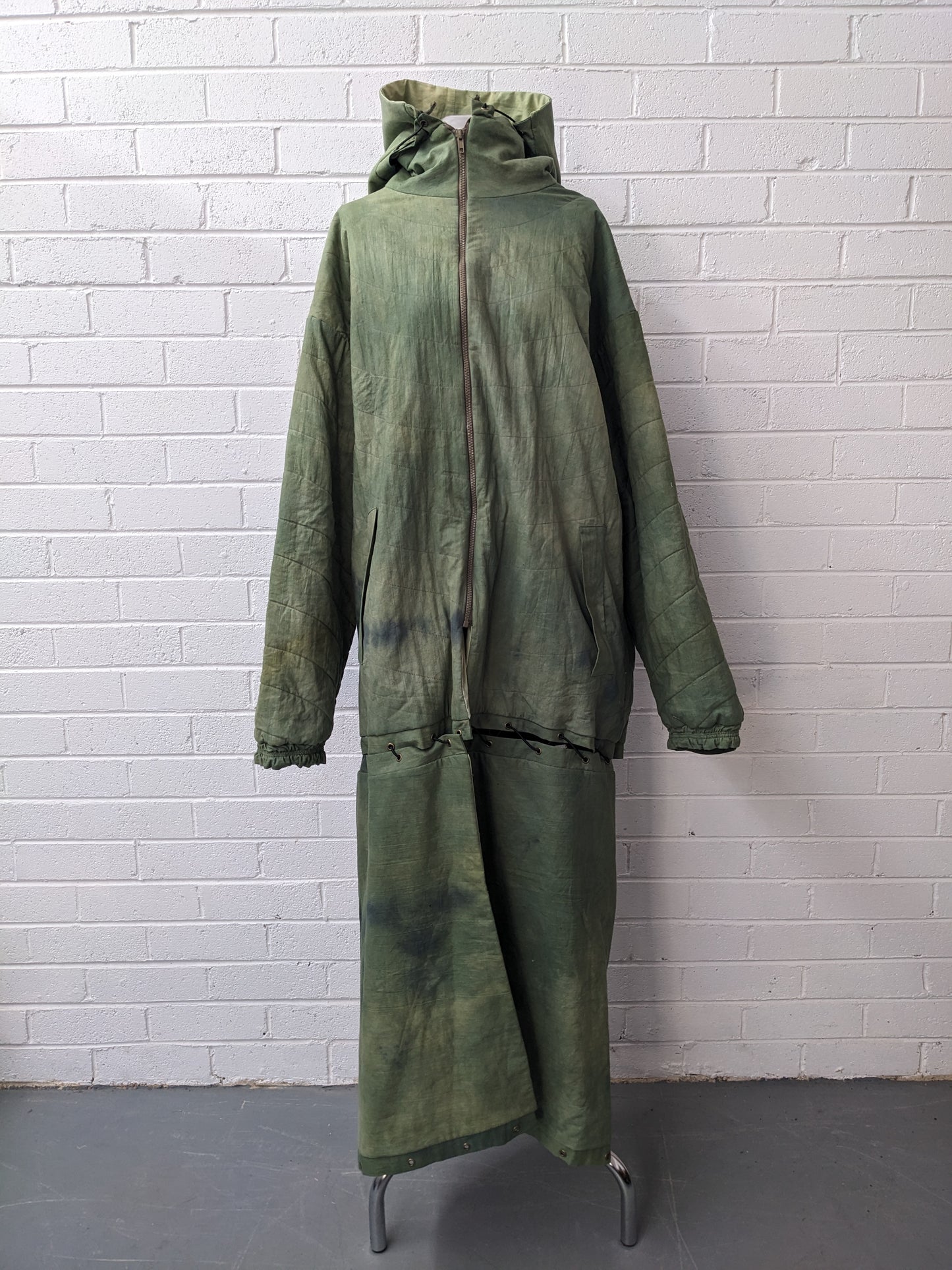 Green modular coat with hood on dress form in front of brick wall