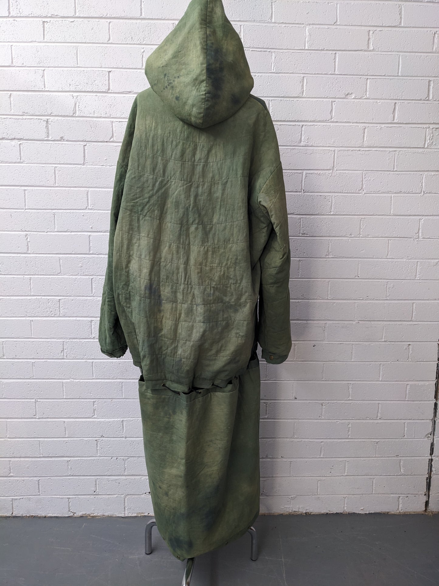 Green modular coat with hood on dress form in front of brick wall