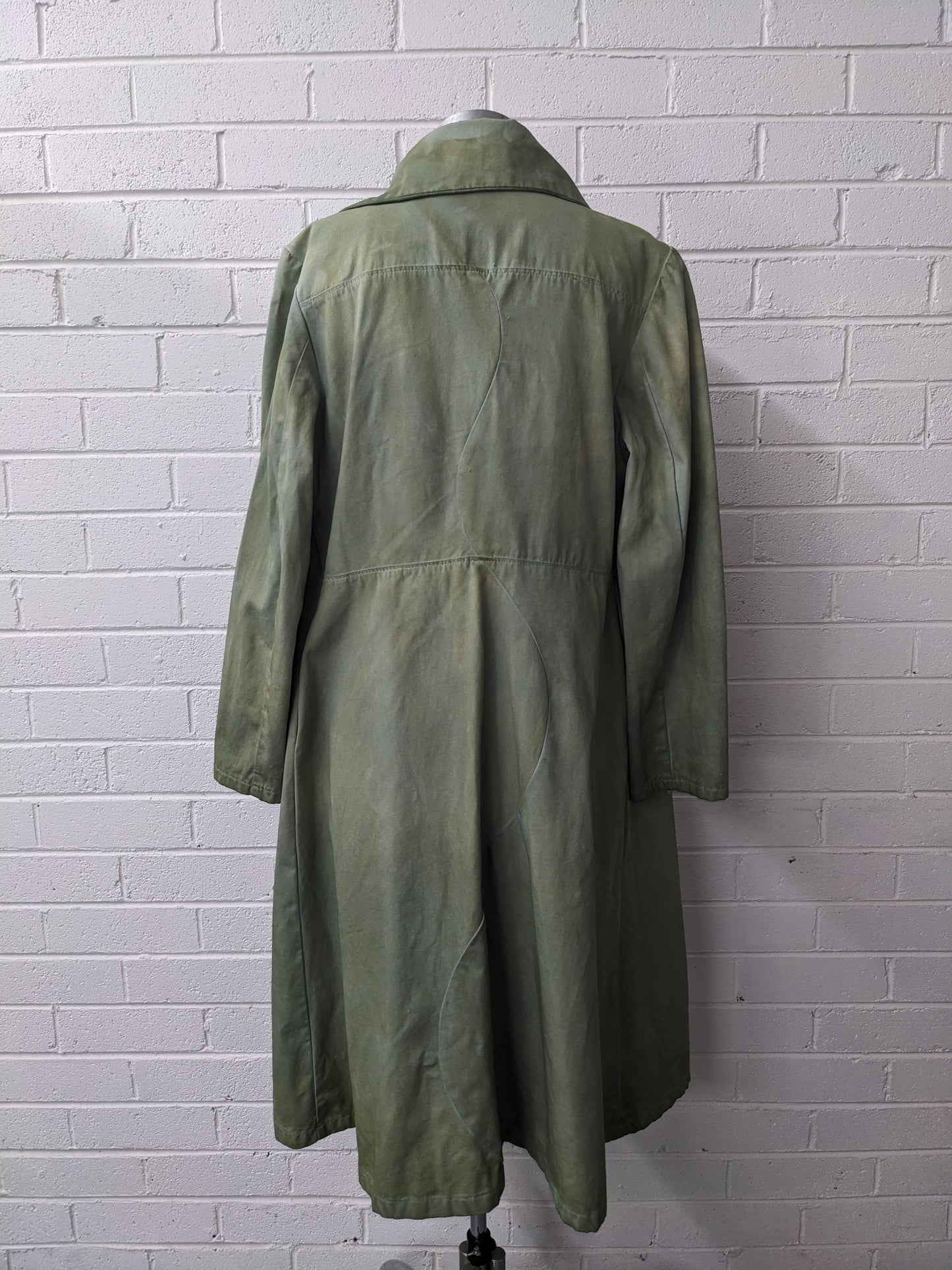 Green coat on a mannequin against a white brick wall