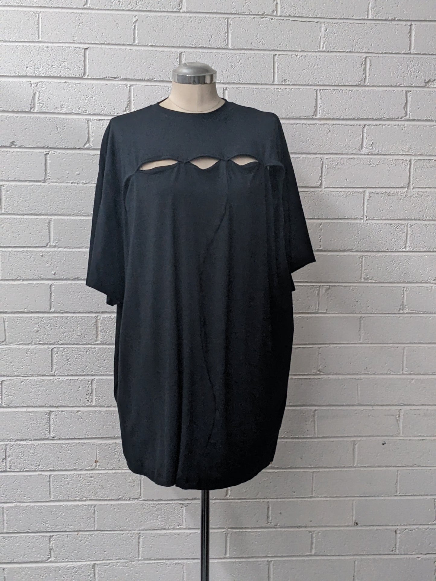 Black t-shirt with cut-out design on a mannequin against a white brick wall.