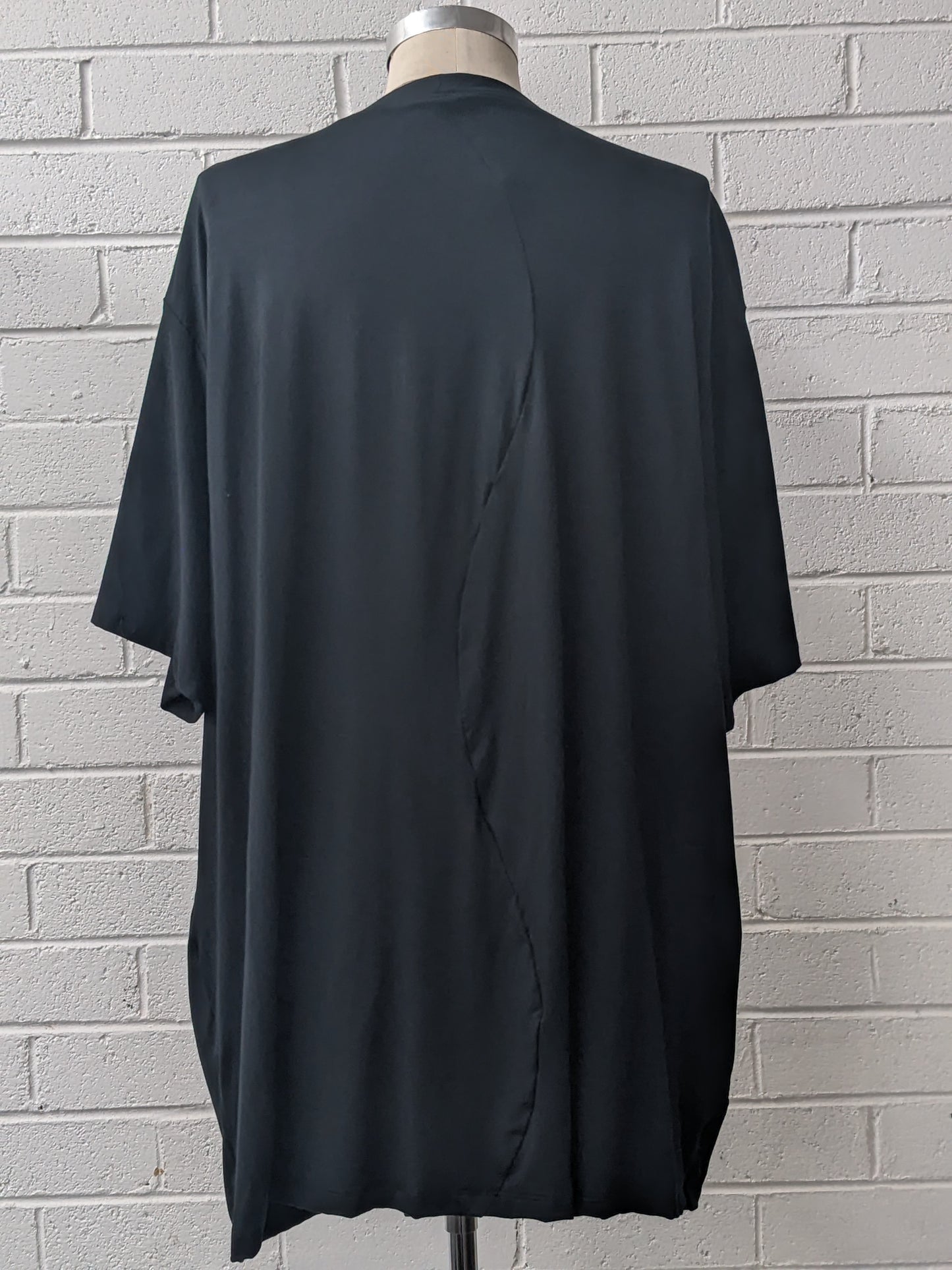 Black t-shirt with cut-out design on a mannequin against a white brick wall.