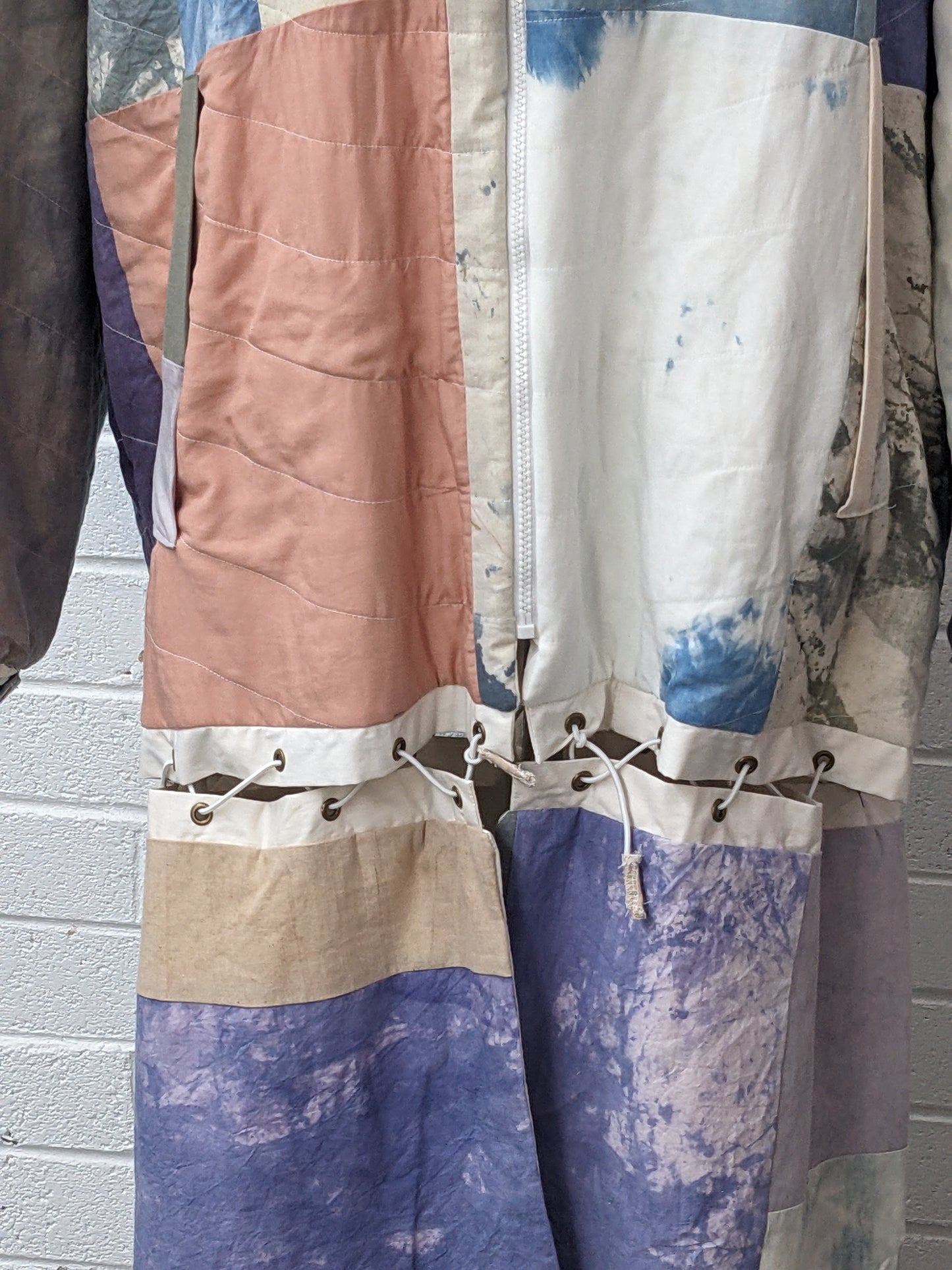 Hand dyed quilted coat on dress form in front of white brick wall