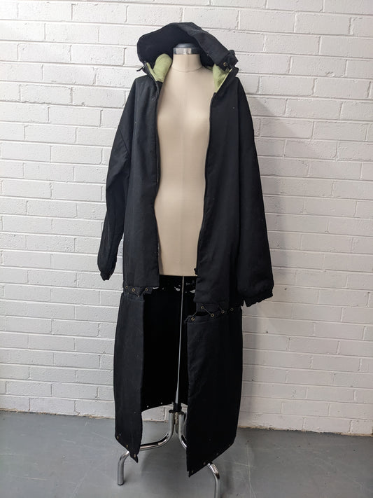 Black modular coat on dress form in front of brick wall 
