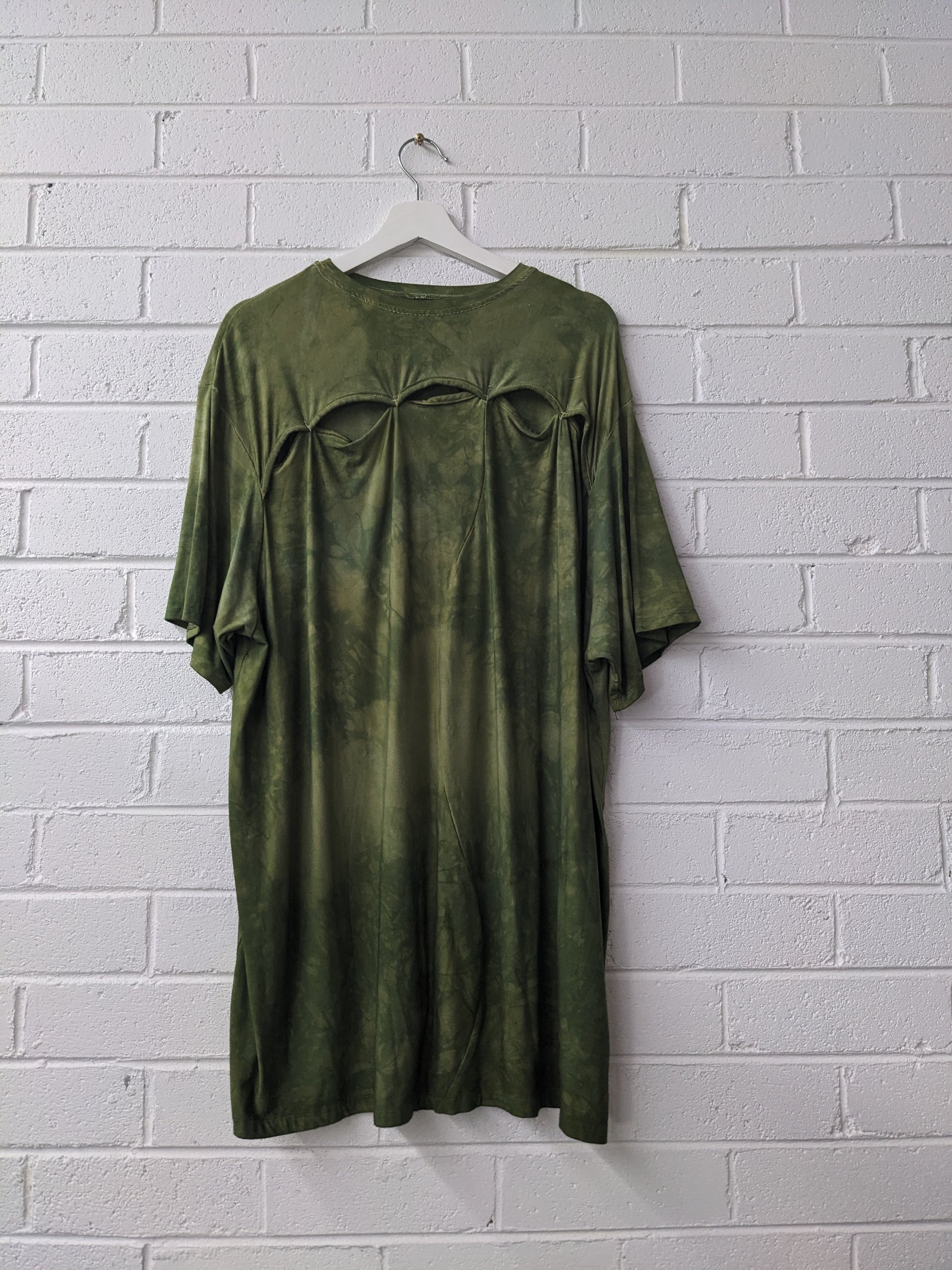 Green dress on a hanger against a white brick wall