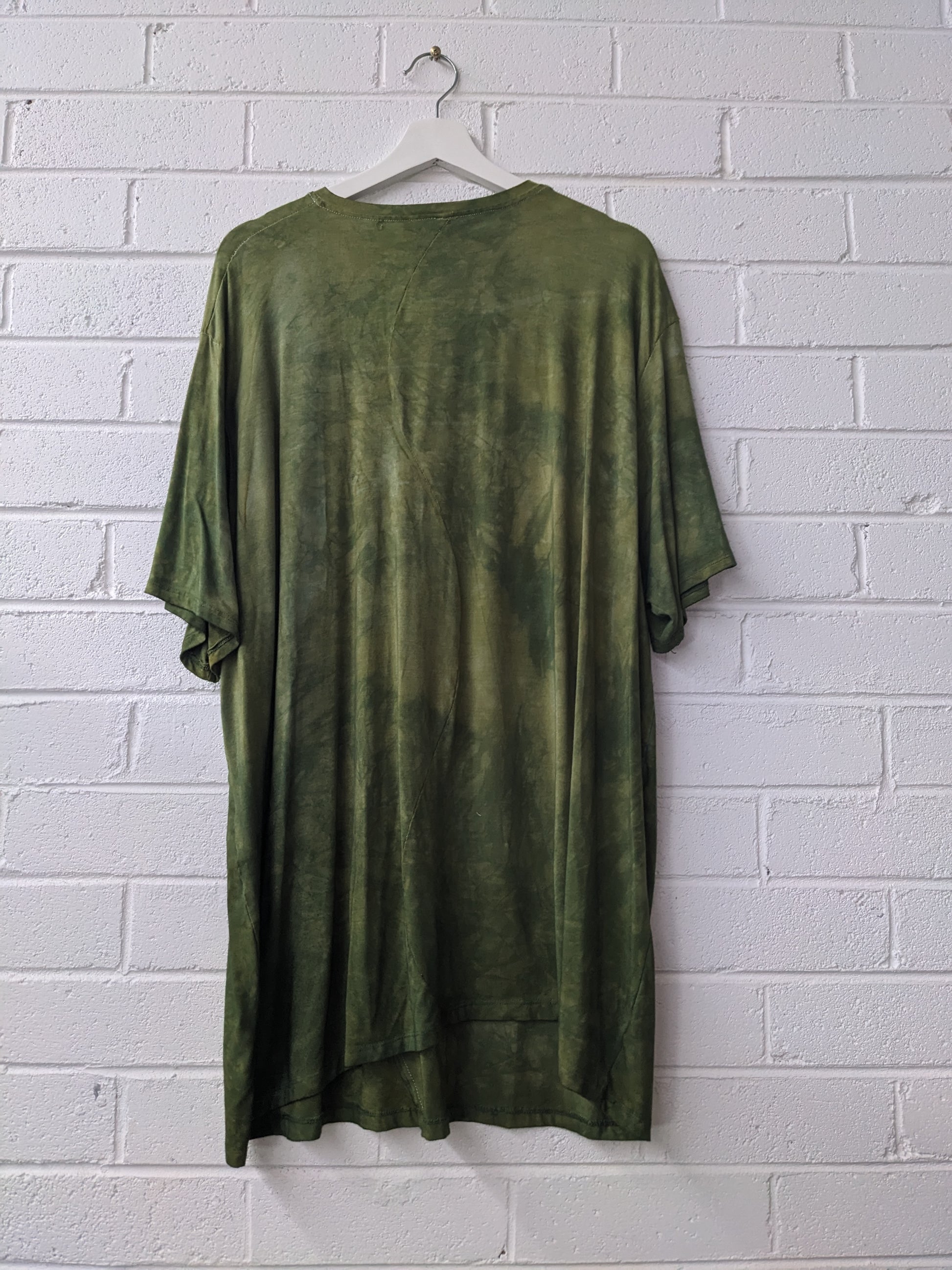 Green t-shirt on a hanger against a white brick wall