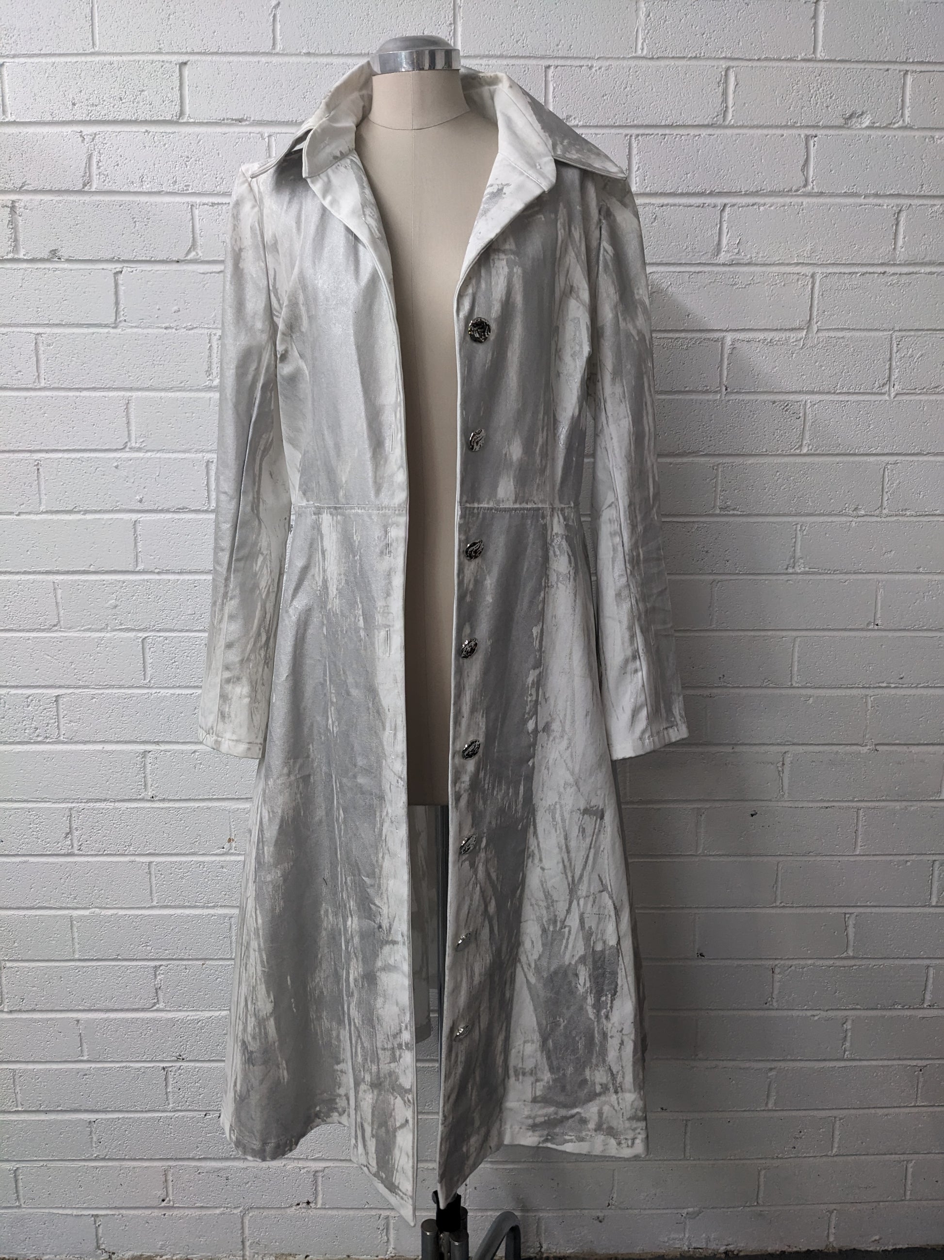 Long silver coat on mannequin against brick wall 