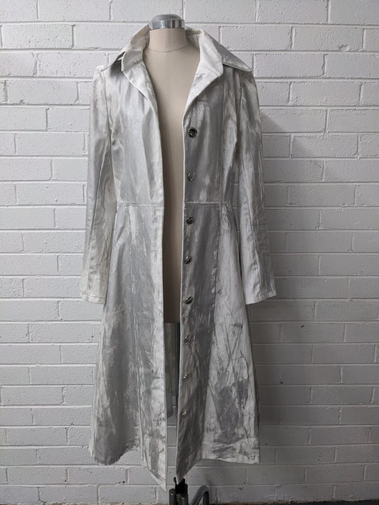 Long silver coat on mannequin against brick wall 
