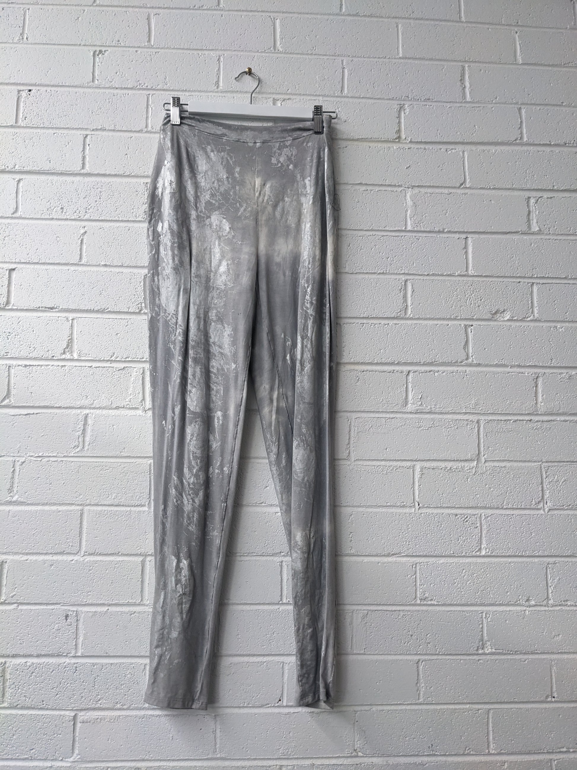 Silver metallic pants hanging against a white brick wall