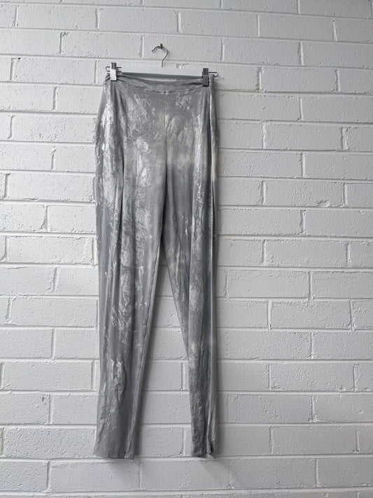 Silver metallic pants hanging against a white brick wall