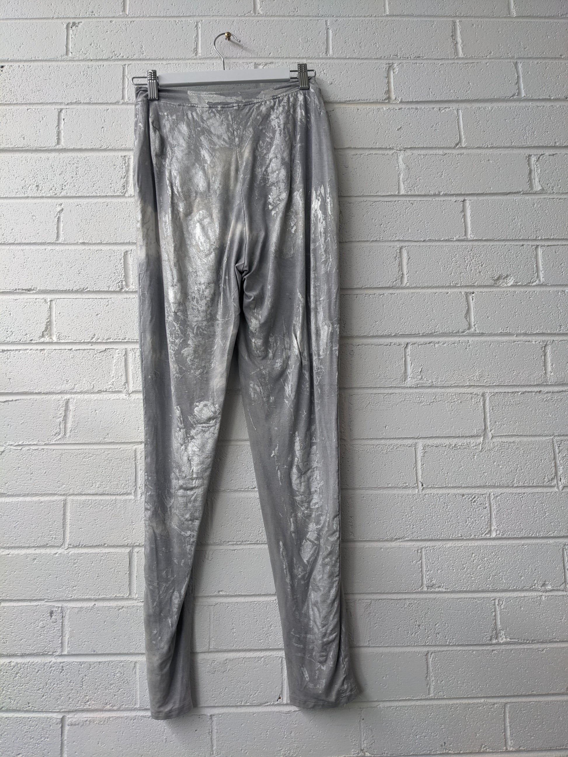 Silver metallic pants hanging against a white brick wall