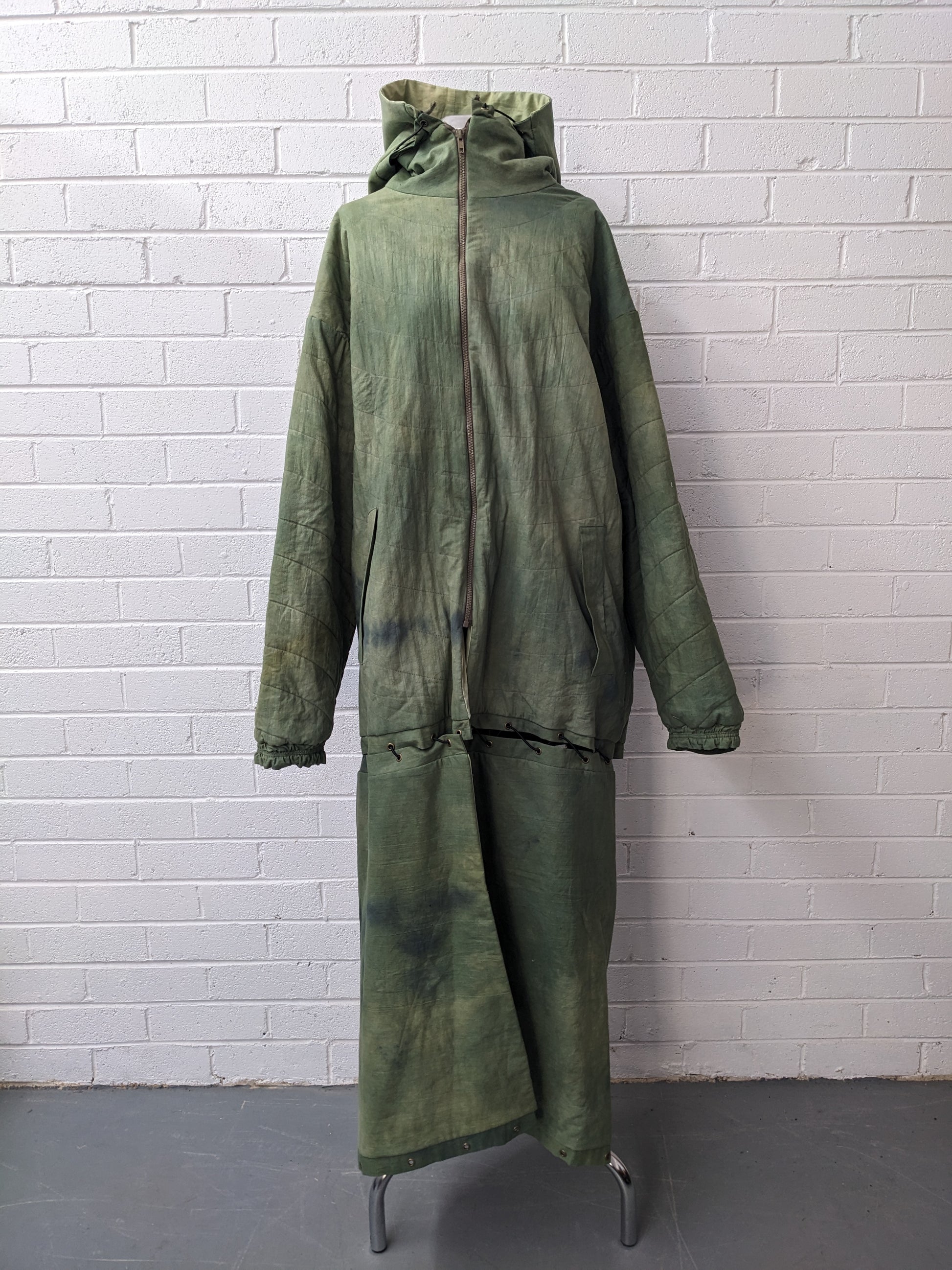 Green modular coat with hood on dress form in front of brick wall 