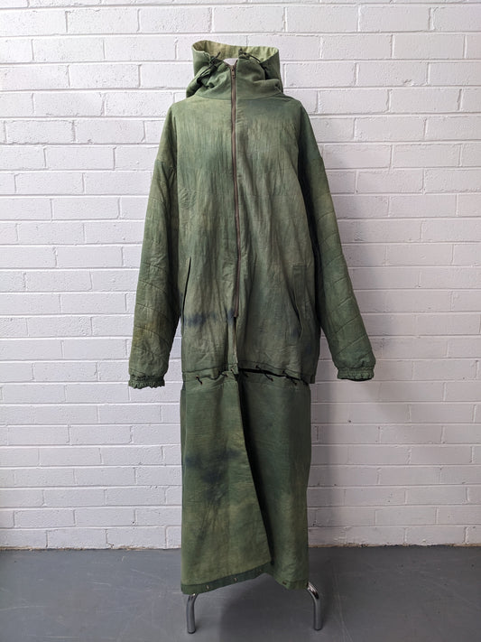 Green modular coat with hood on dress form in front of brick wall 