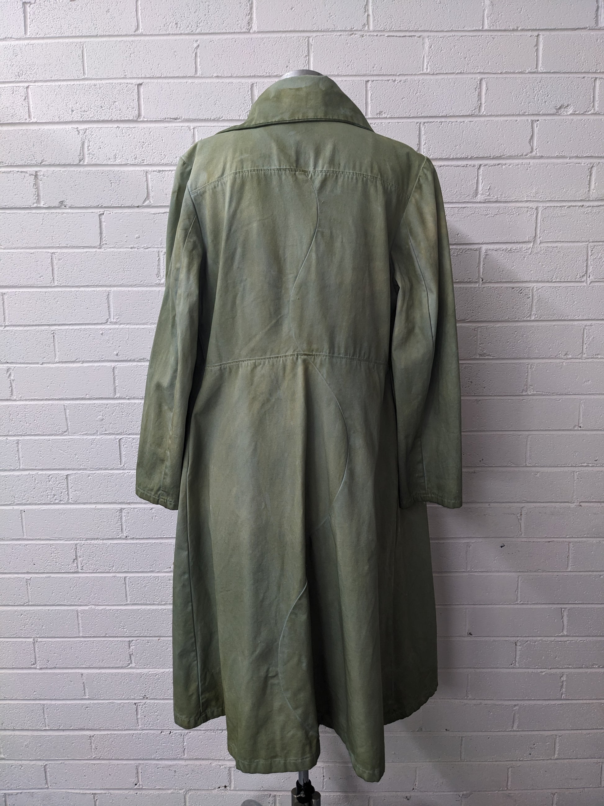 Green coat on a mannequin against a white brick wall