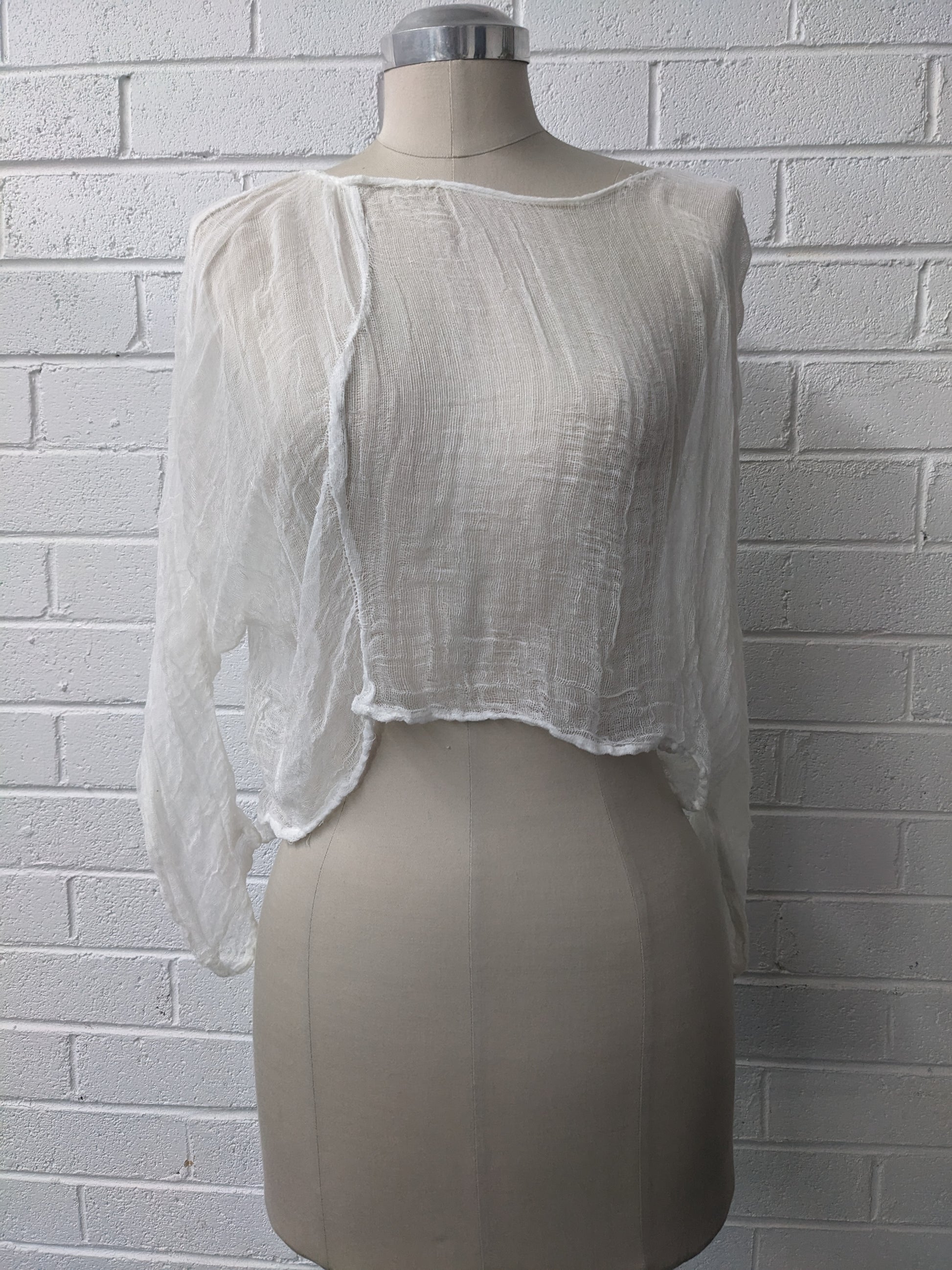 White sheer blouse on a mannequin against a white brick wall.