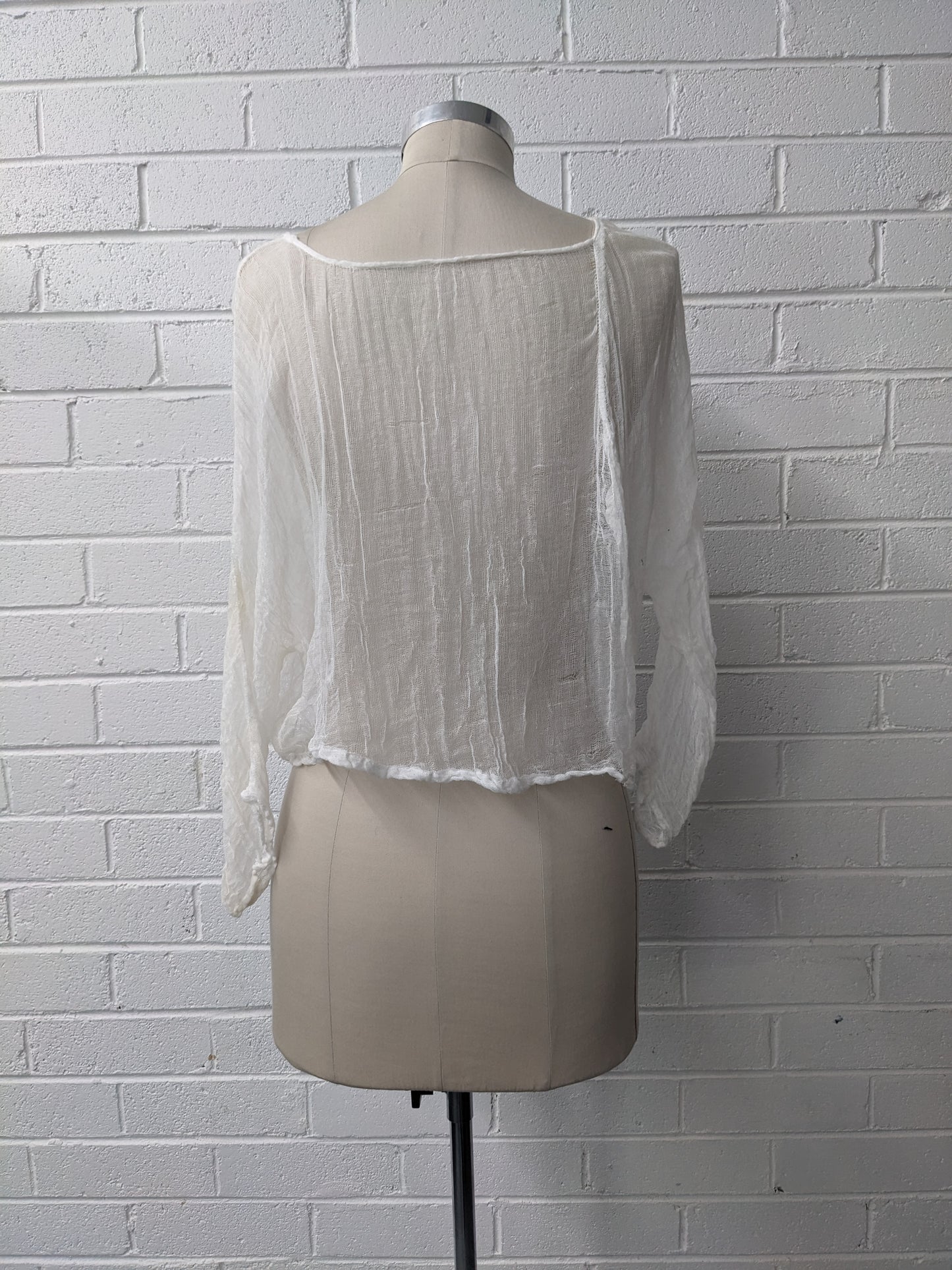 White sheer blouse on a mannequin against a white brick wall.