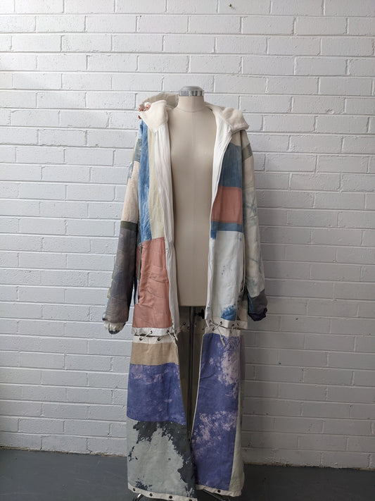 Hand dyed quilted coat on dress form in front of white brick wall 